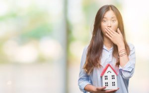 Young asian woman real state agent holding house isolated background cover mouth with hand shocked with shame for mistake, expression of fear, scared in silence, secret concept
