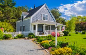 An American flag flies from the open porch and gardens surround a small single family home on a Spring afternoon on Cape Cod on the Massachusetts coast.