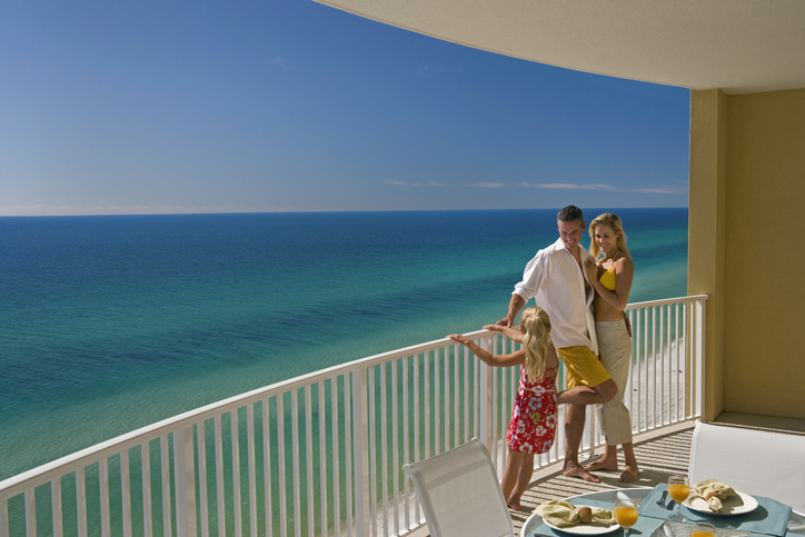 Mom, dad and daughter standing on the balcony overlooking Gulf of Mexico.