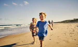 Shot of two adorable little children running at the beach with their parents in the background